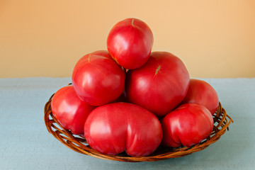Ripe very large tomatoes in a wooden basket on a colored background