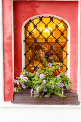 Fototapeta na wymiar Window with lattice in old brick wall, flowers on the windowsill.