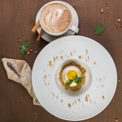 Mango cake, mousse dessert on a white plate with cup of coffee cappuccino on the brown table. Top view.
