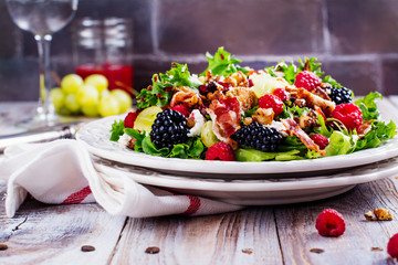 Delicious summer salad with mix of berries, nuts, feta chees, bacon and raspberry sauce on vintage background. Space for text