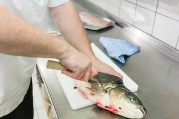 Chef in restaurant kitchen filleting carp fish, close-up