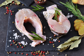Steak of white fish on a black stone background with spices and rosemary.
