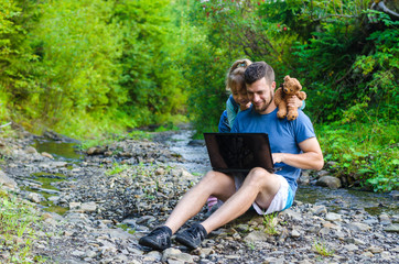 Dad and daughter are looking at the laptop, sitting on the nature, free space for your text.