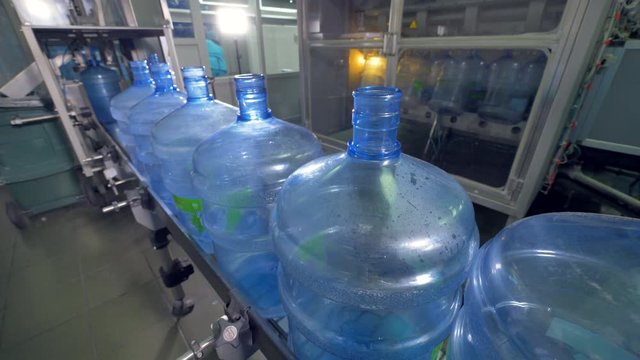 Groups of huge empty water bottles move on a conveyor line. 4K.