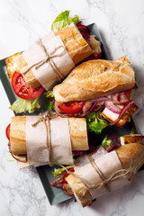 Fresh baguette sandwich bahn-mi styled. Bacon, roasted cheese, tomatoes and lettuce on metallic tray on white marble background.