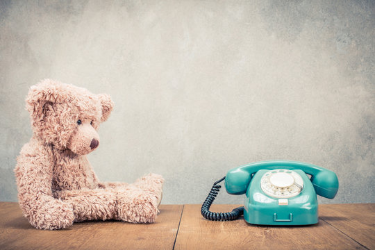 Teddy Bear toy and old retro mint green rotary telephone front concrete wall background. Vintage instagram style filtered photo