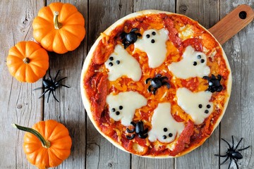 Fototapeta premium Halloween pizza with ghosts and spiders, above scene with decor on a rustic wood background