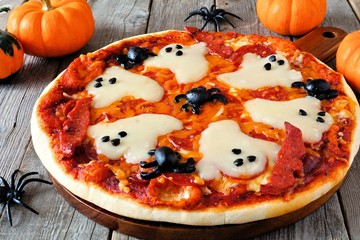Halloween pizza with ghosts and spiders, close up on a rustic wood background
