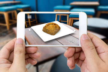 Augmented reality marketing technology concept. Customer hand holding smart phone use AR application to select menu in restaurant. 3d rendering of bread can move 360 degrees for see around object.