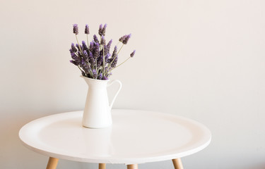 Purple lavender in small white jug on round table against neutral wall