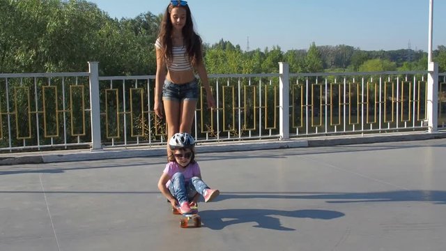 The child swings sitting on the skateboard. Falling baby from the skateboard. Happy sisters on wheels.