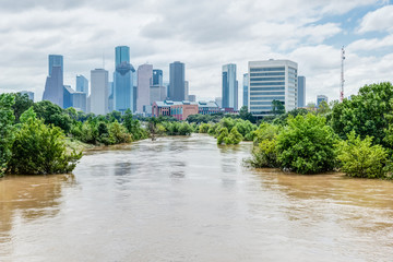 High and fast water rising in Bayou River with downtown Houston in background under cloud blue sky....