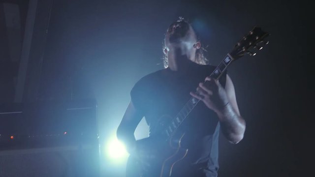 Concert rock band performing on stage with guitarist. man plays the electric guitar. Music video punk, heavy metal or rock group.