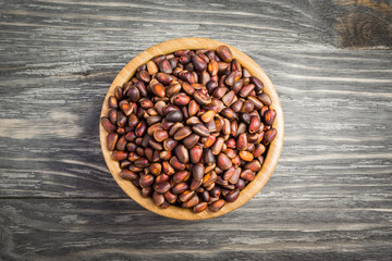 Unpeeled pine nuts in a wooden bowl on wooden background. Top view, space for text.
