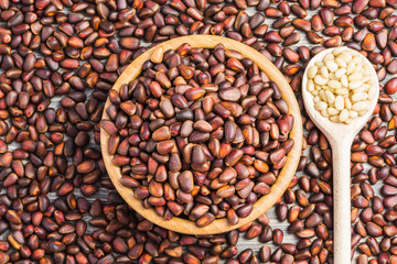 Unpeeled pine nuts in a wooden bowl on wooden background.  Top view.