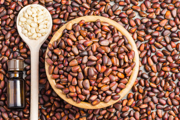 Unpeeled pine nuts in a wooden bowl, wooden spoon with unpeeled nuts and a bottle with essential oil. Top view, space for text. 