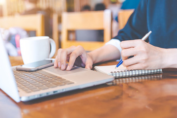 Business woman hand is working on a notebook computer and writing on a note pad with a pen. © apichon_tee