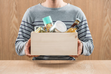 Volunteer with donation box with food stuffs on wooden background