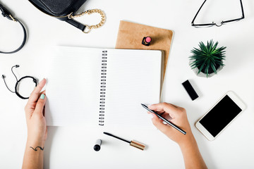 Woman hands writing in notebook on white table with female accessories