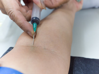 Close up of clinician hand collecting blood for blood test using needle and syringe puncture on left patient forearm at hospital