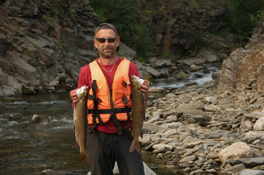 Fisherman holding two large asiatic trouts on the shore of the wild Siberian river.