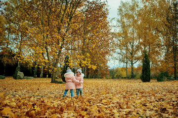 Fototapeta premium Two happy children playing in autumn clothes in the park. Little sister girls sitting on yellow leaves in nature.