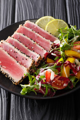 Seared ahi tuna coated sesame seeds with salad on black plate closeup. vertical