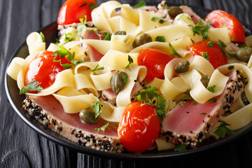 Mediterranean cuisine: fettuccine pasta with tuna in sesame, with tomatoes and capers close-up. horizontal