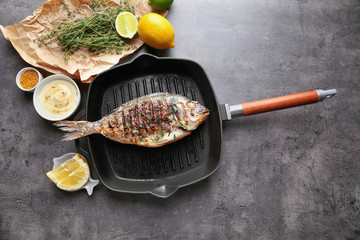 Frying pan with delicious prepared fish and ingredients on table