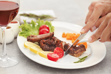 Young man eating delicious ribs in restaurant, closeup