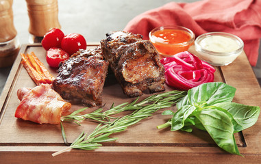 Delicious roasted ribs and ingredients on wooden board, closeup