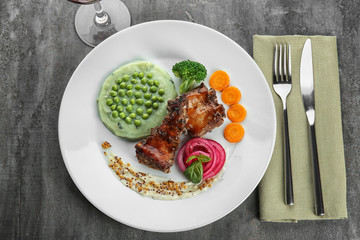 Plate with delicious ribs, vegetables and mushy peas on table