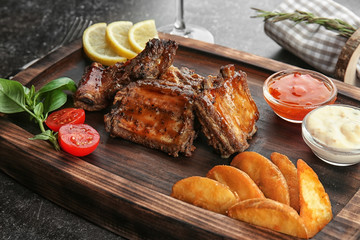 Wooden tray with delicious ribs and vegetables, closeup