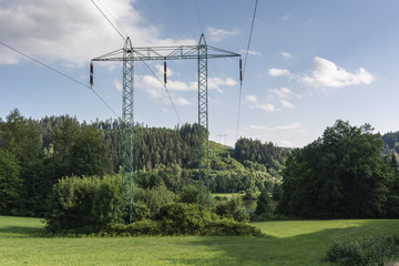 High voltage metal pillars in landscape and hill in the background.