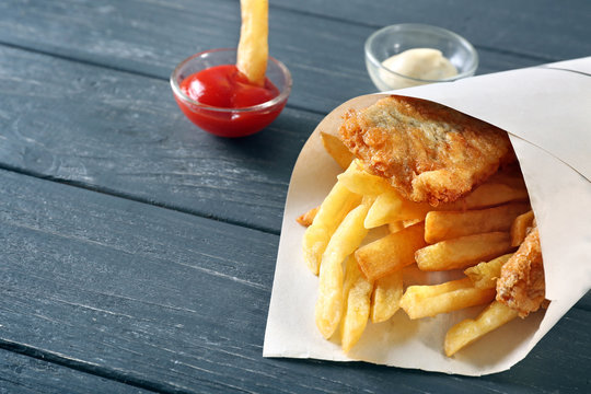 Fried fish and chips in a paper cone on wooden background