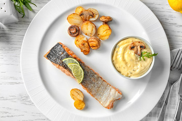 Plate with slice of delicious salmon and fish sauce on table