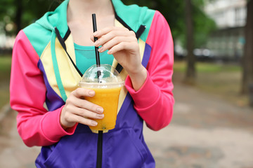 Woman in sport suit holding yellow smoothie outdoors