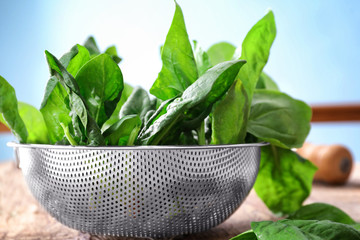 Colander with fresh spinach leaves on table