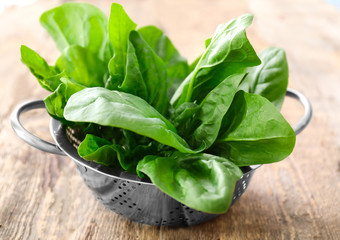 Colander with fresh spinach leaves on table