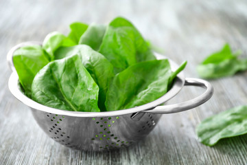 Colander with fresh spinach leaves on table