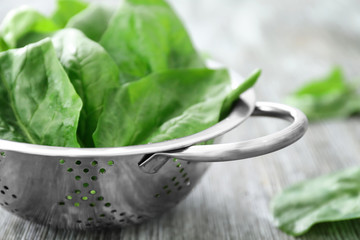 Colander with fresh spinach leaves on table
