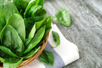 Wicker basket with fresh spinach leaves on table