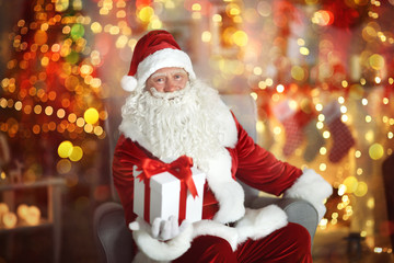 Santa Claus holding gift box in room with beautiful Christmas decorations