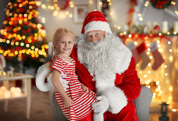 Fototapeta na wymiar Little girl sitting on Santa's lap in room with beautiful Christmas decorations