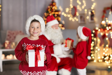 Fototapeta na wymiar Cute boy holding gift box in room with beautiful Christmas decorations
