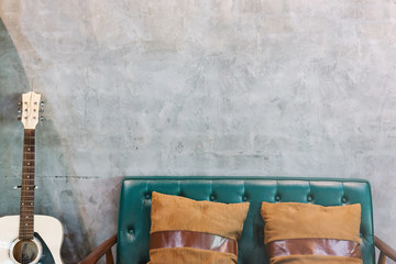 two brown pillows on sofa and white guitar place at the concrete or loft wall in the room.