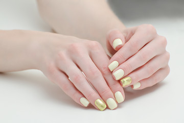 Beautiful female hands with a manicure on a light background. Yellow with gold nails
