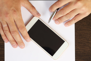 Hands, phone, white paper on the desktop, top view close-up