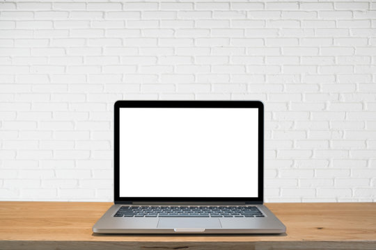Laptop computer with blank screen on wooden table and white bricks wall background