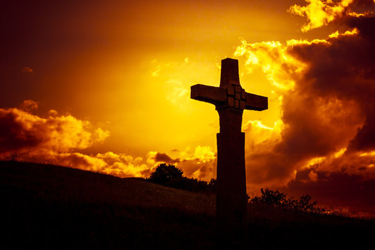 a stone cross in front of a dramatic evening sky